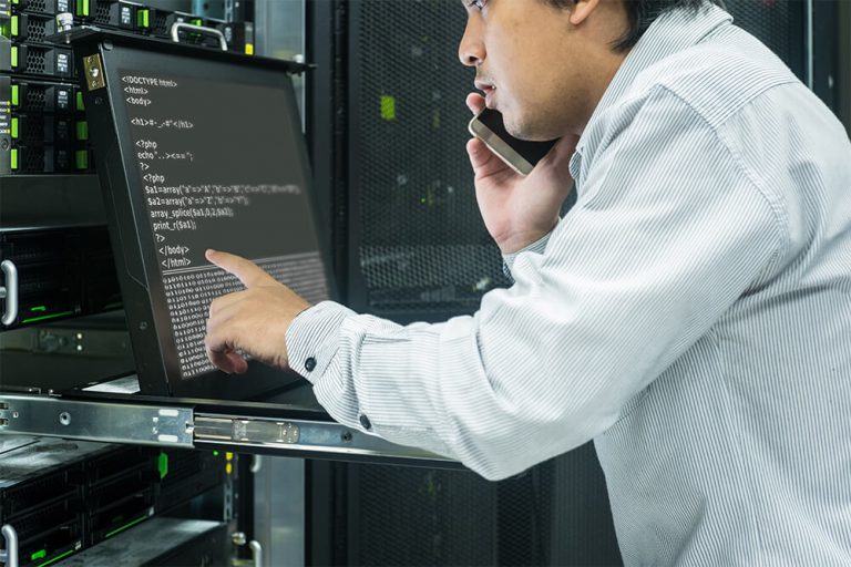 IT person in server room pointing to laptop screen on phone