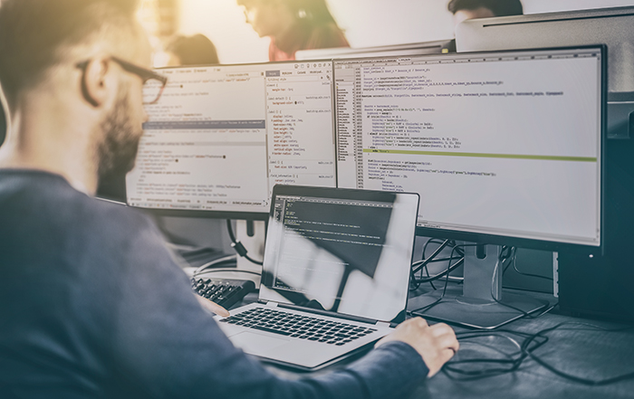 man at laptop with 2 monitors in background